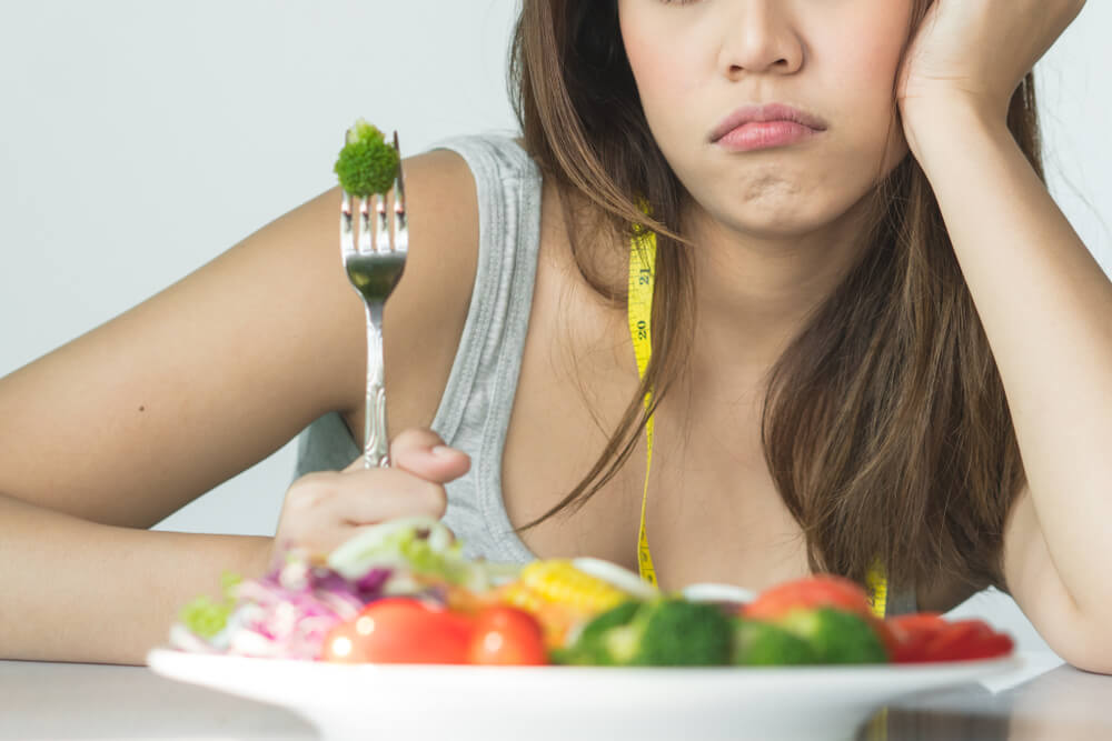 Une jeune femme qui boude devant une assiette de légumes. 