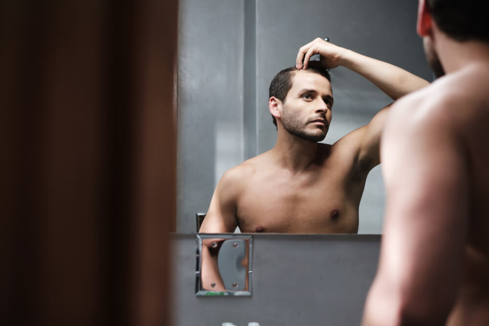 Un homme qui regarde ses cheveux dans un miroir. 
