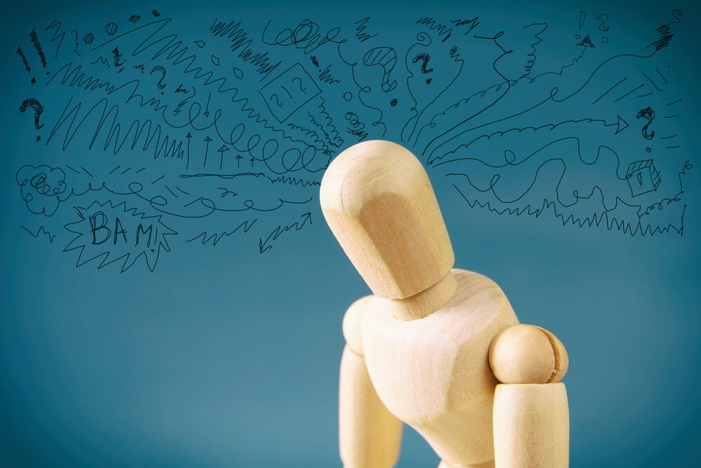 A wooden figure looking downtrodden, with scribbles and symbols written around its head.