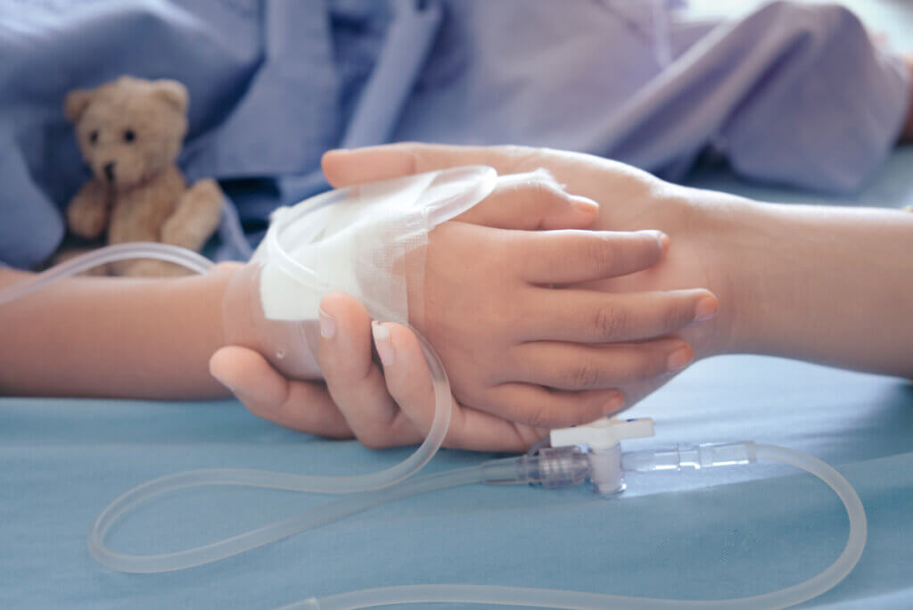 A child in a hospital bed holding their caregiver's hand.