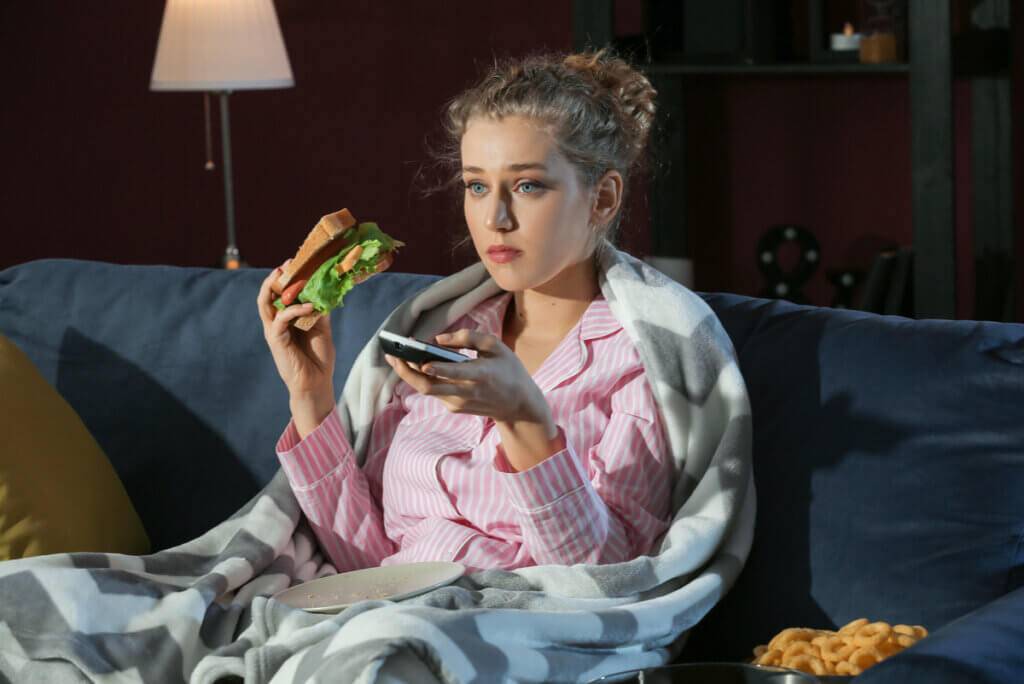 A woman eating a sandwich and watching TV late at night.