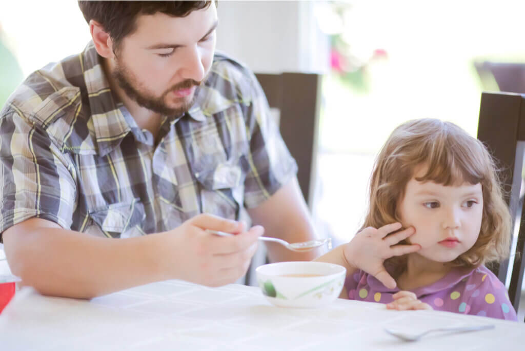 A father trying to offer his daughter a spoonful of soup.