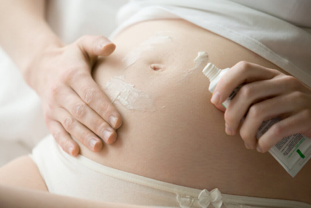 A pregnant woman spreads lotion on her belly.