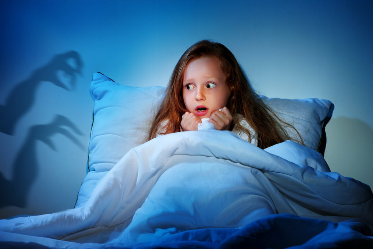 A young girl that's sitting up scared in her bed because she thinks she sees a monster.