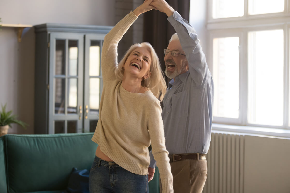 An older couple dancing and laughing in their living room.