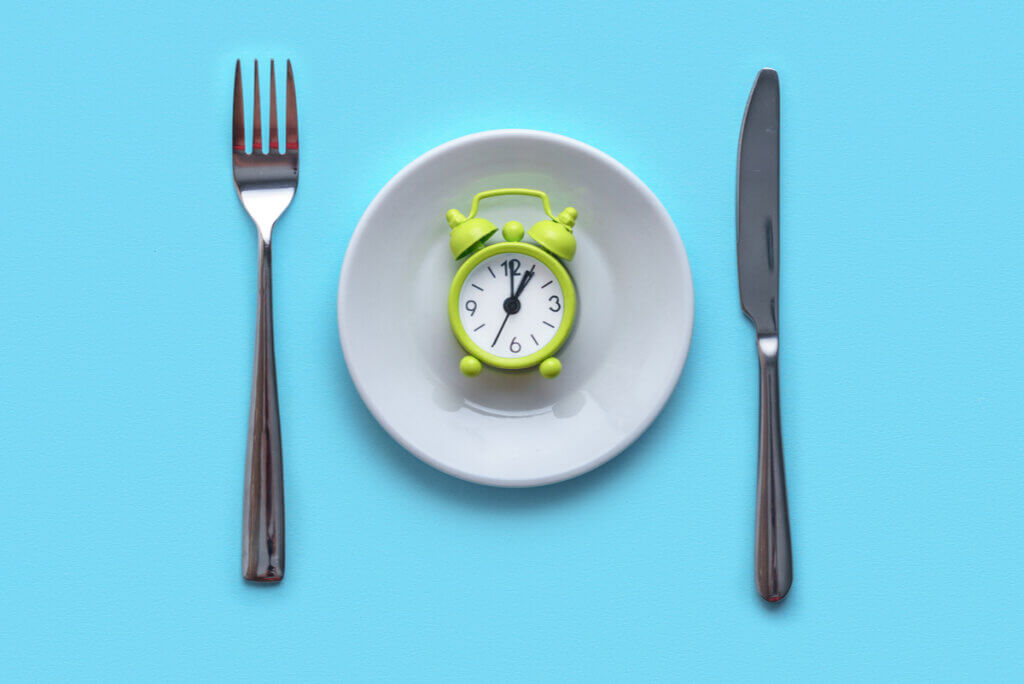 A place setting with a tiny alarm clock in the middle of the plate.