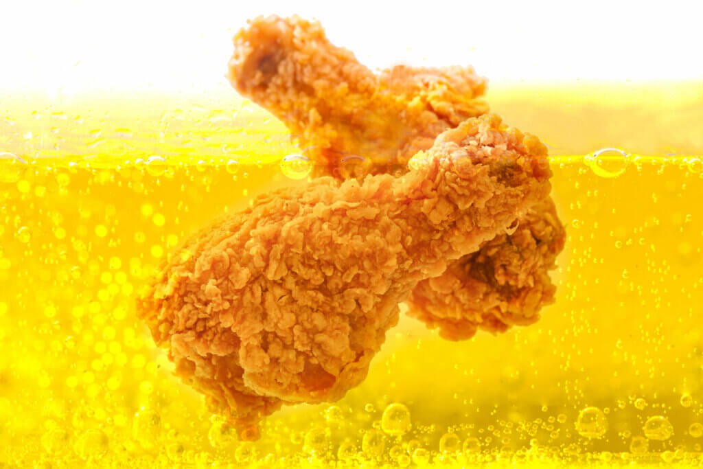 Battered chicken drumsticks frying in oil.