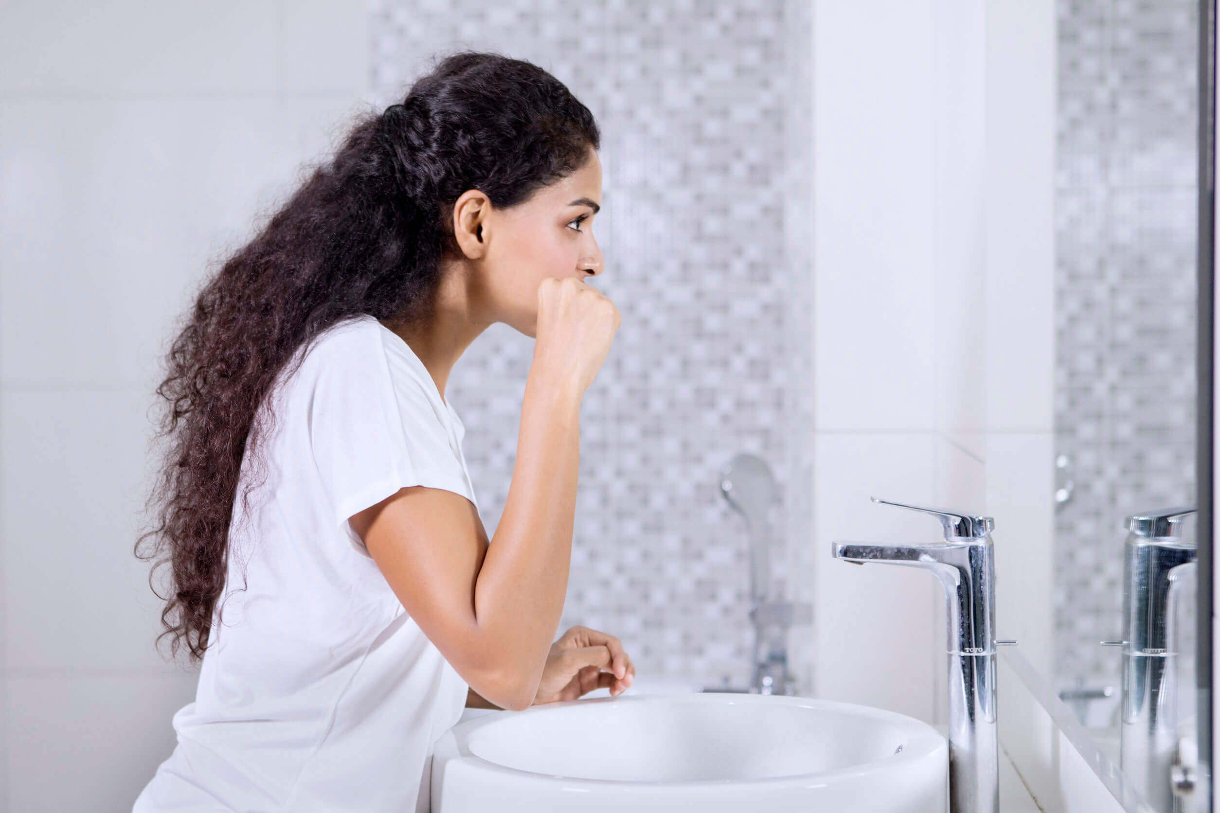 A woman looking in the mirror and brushing her teeth.