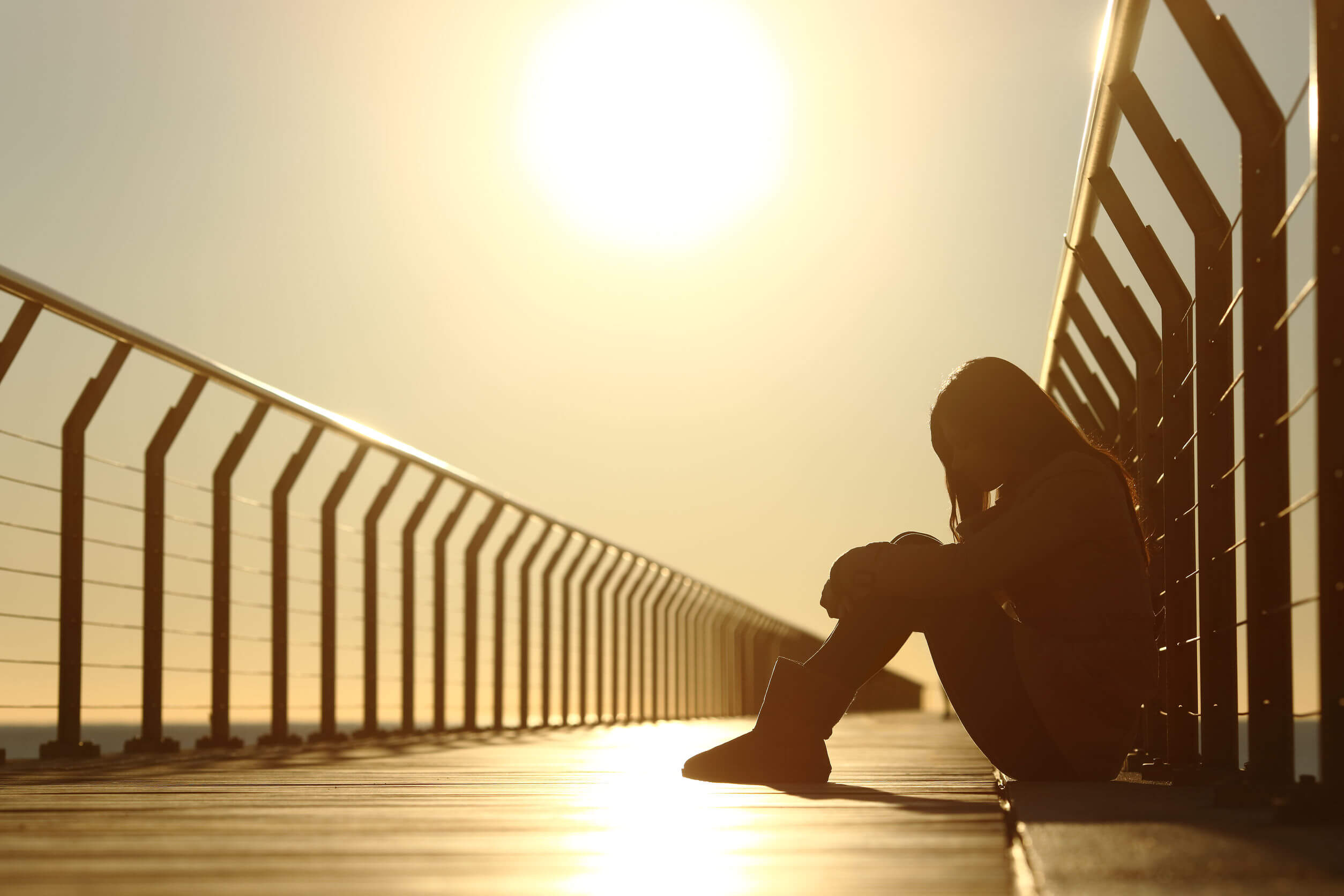 A depressed woman sitting on a bridge.