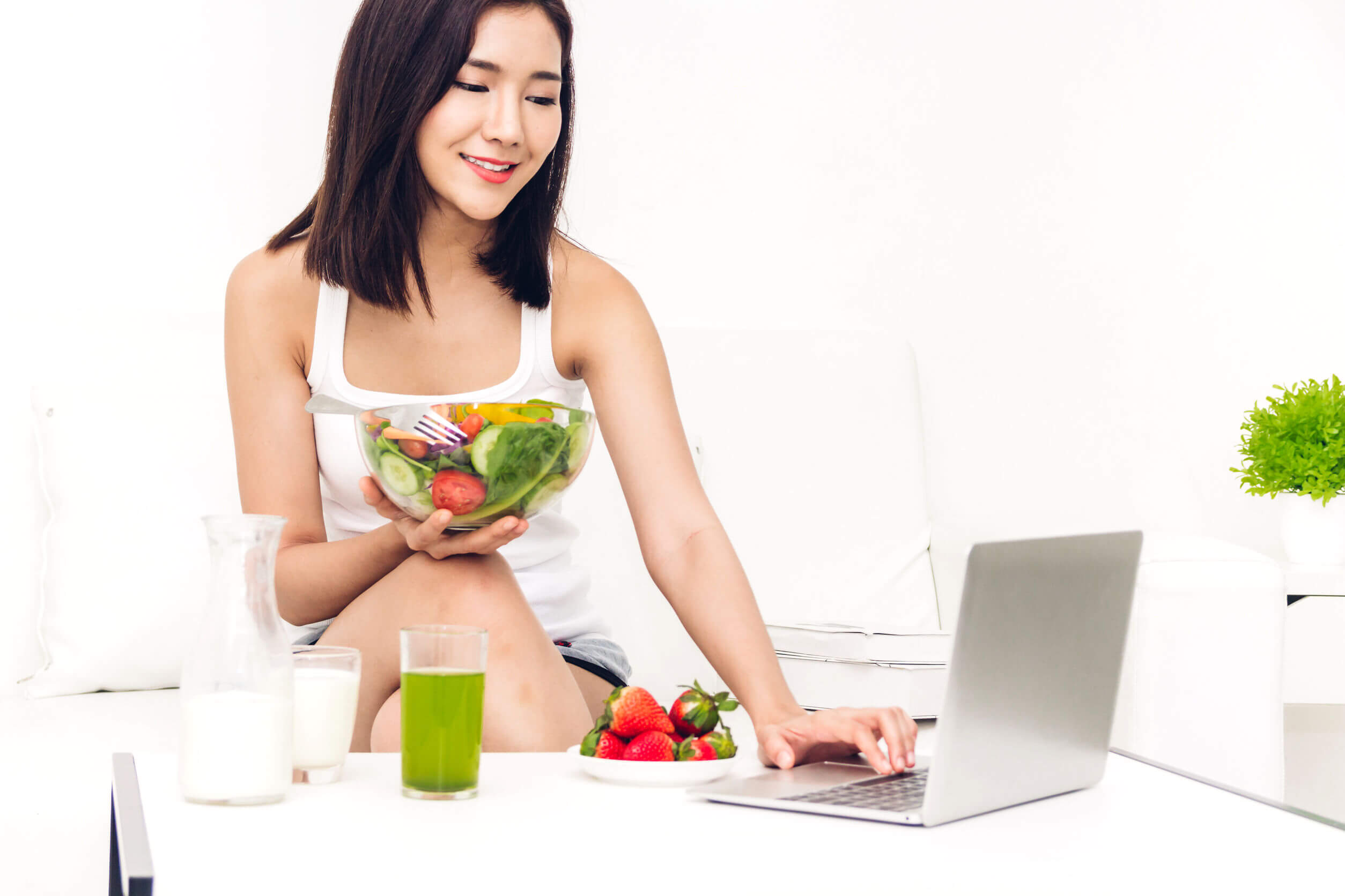 A young Asian women eating a fresh fruits and vegetables while working on her computer.