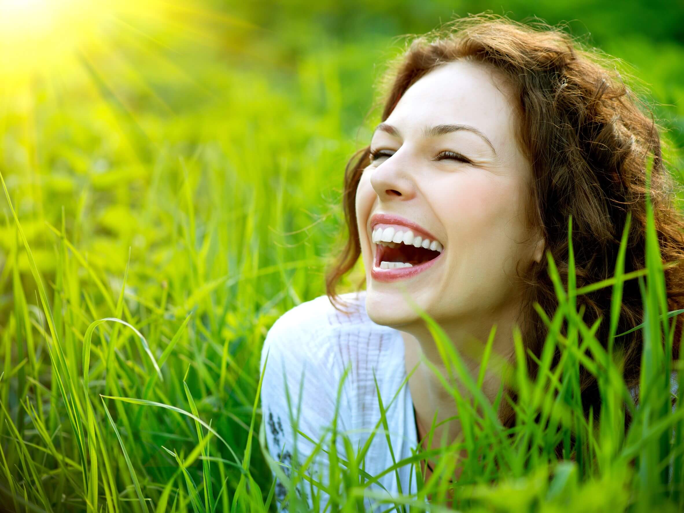 A woman sitting in a field laughing.