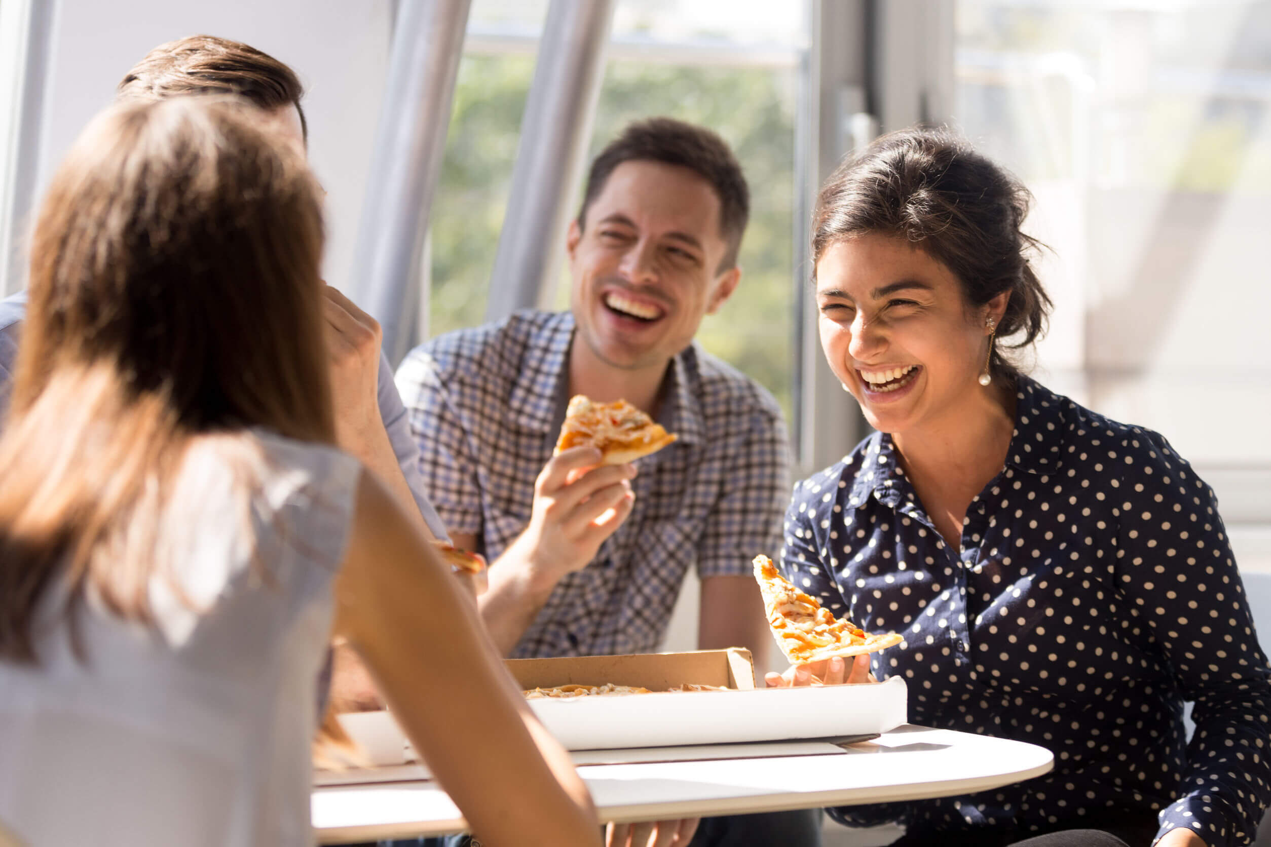 Four friends laughing as they share a pizza.