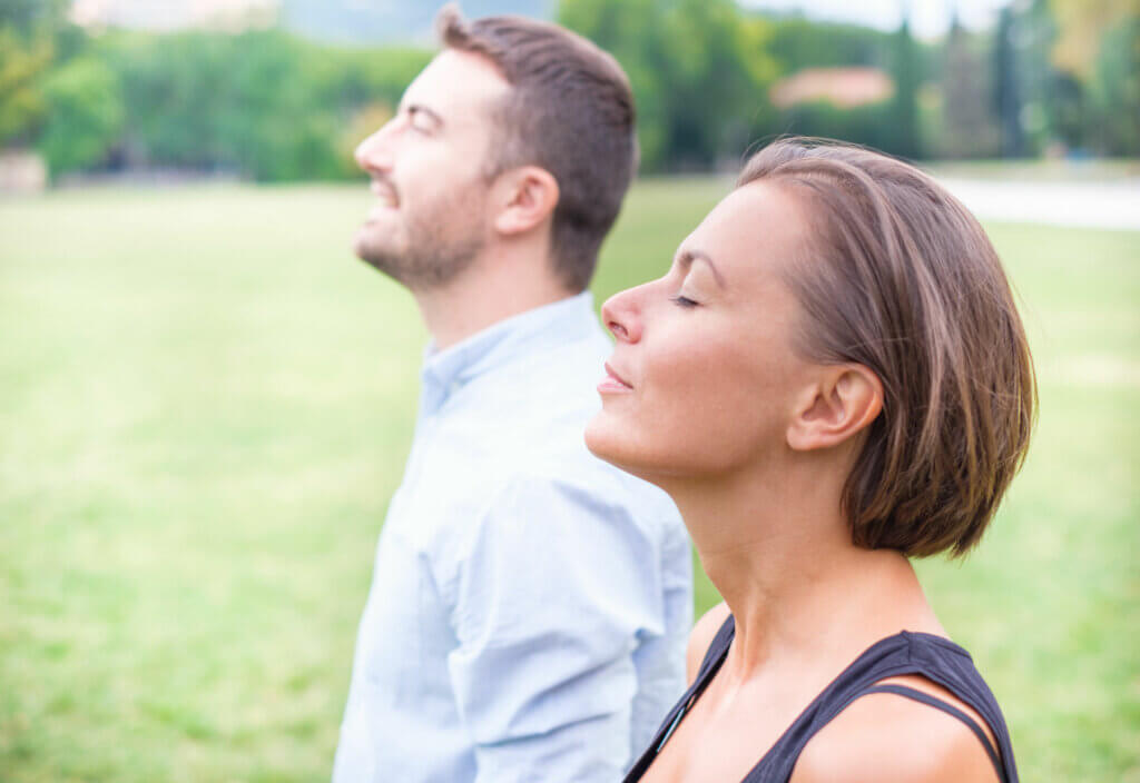 A man and woman standing in a field, practicing breathing techniques.