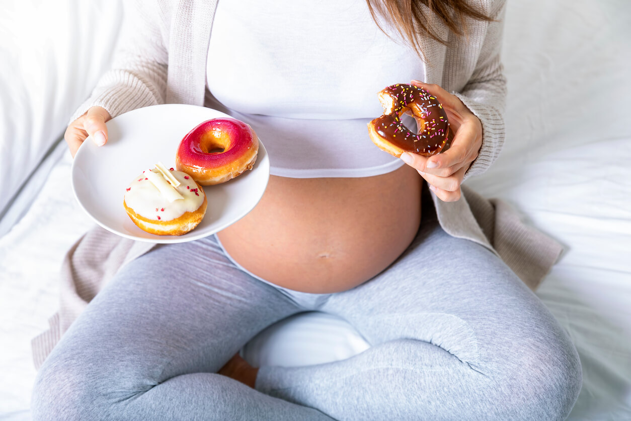A pregnant woman eating plateful of donuts.