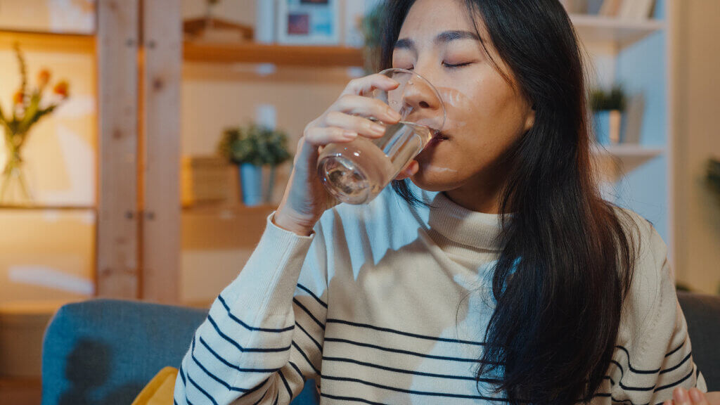 An Asian woman drinking a glass of water.
