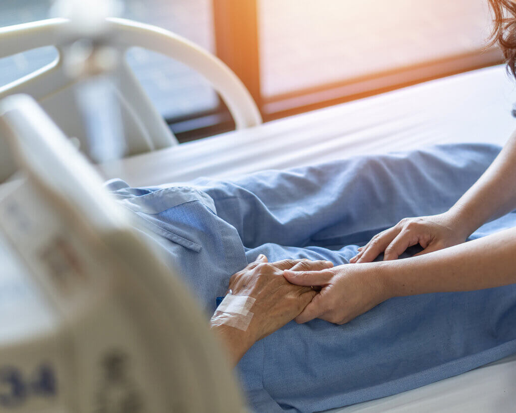 A person holding the hand of a comatose patient.