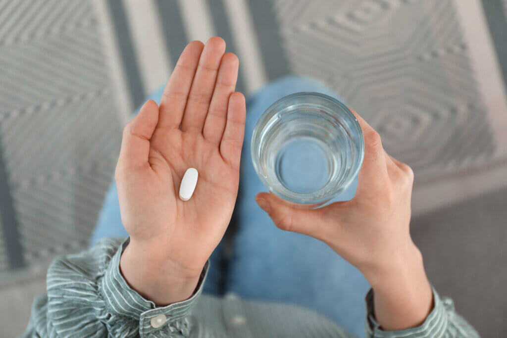 Un médicament dans une main, avec un verre. 