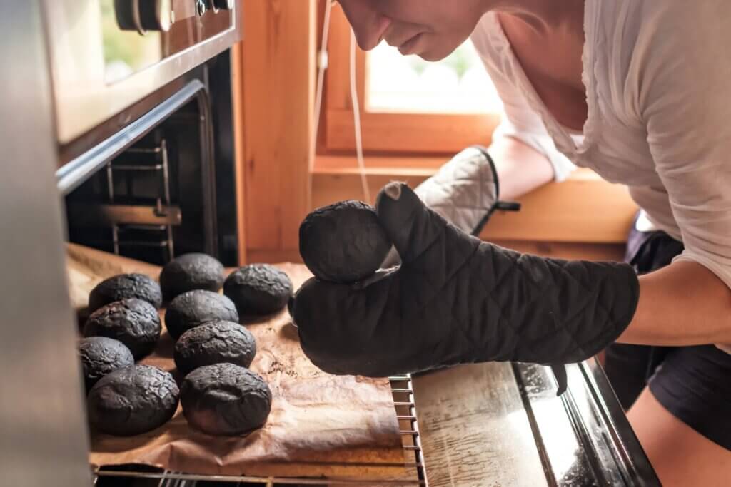 A woman taking burnt bread out of the oven.