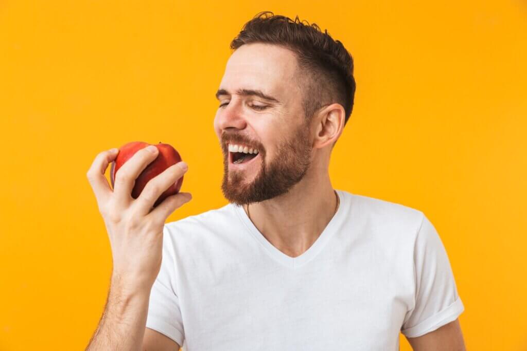 A man smiling as he's about the bite into a red apple.