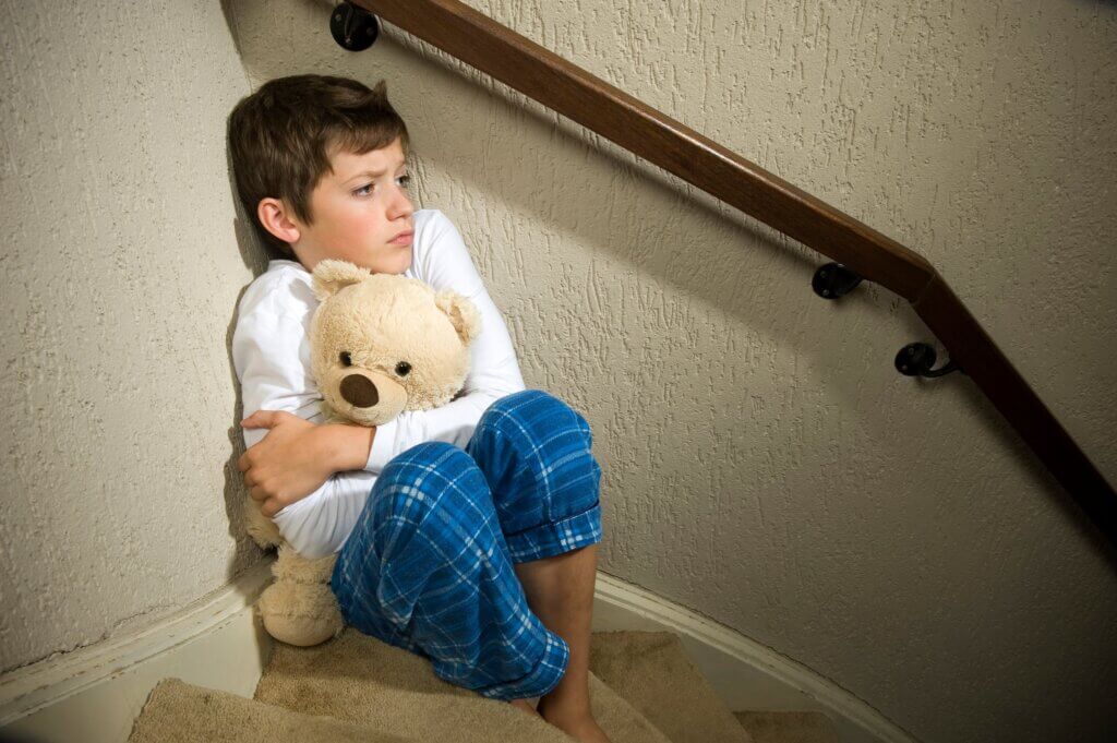 A child sitting on a staircase looking lonely while hugging a teddy bear.