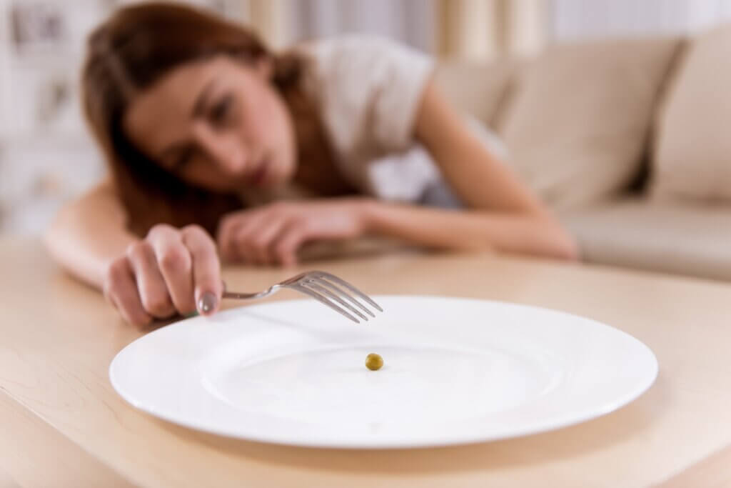 A woman eating a single pea off of an otherwise empty plate.