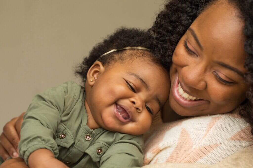 A black woman snuggling her baby as both smile.