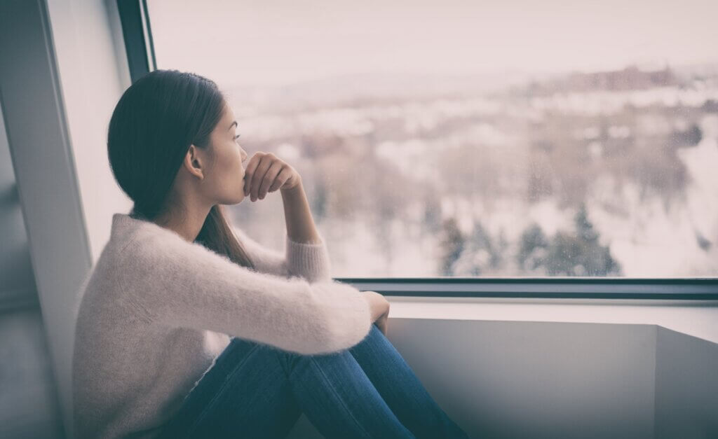 A woman looking sadly out the window at a gray winter landscape.