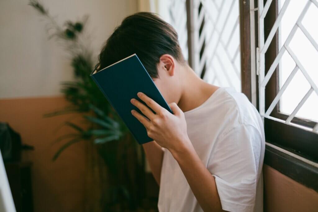 Een kind verstopt zich achter een boek omdat hij verlegen is