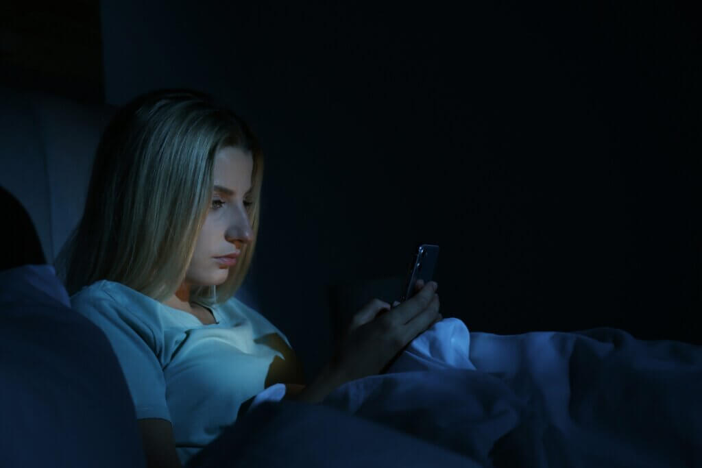 A woman lying in bed looking at her cell phone during the night.