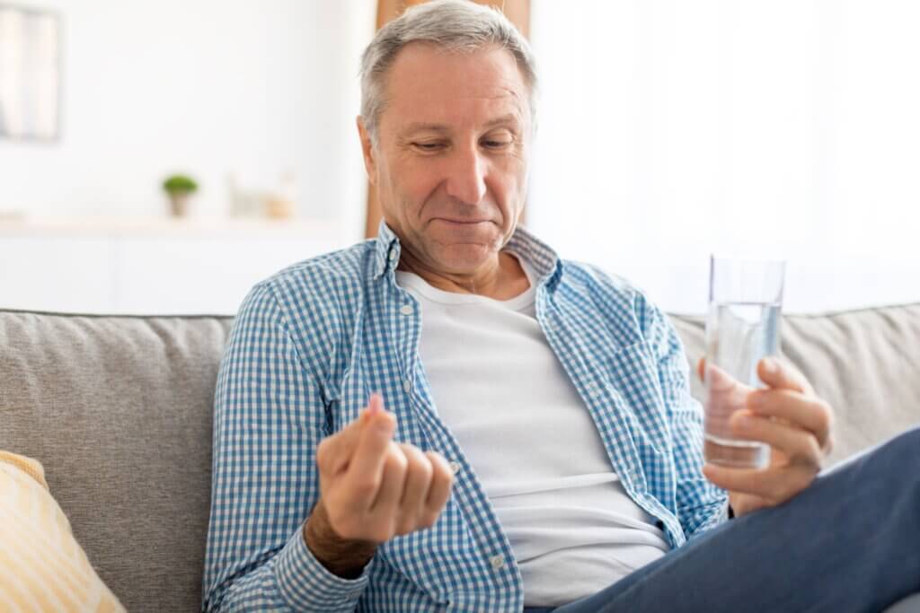 Un homme âgé qui prend un supplément avec un verre d'eau. 