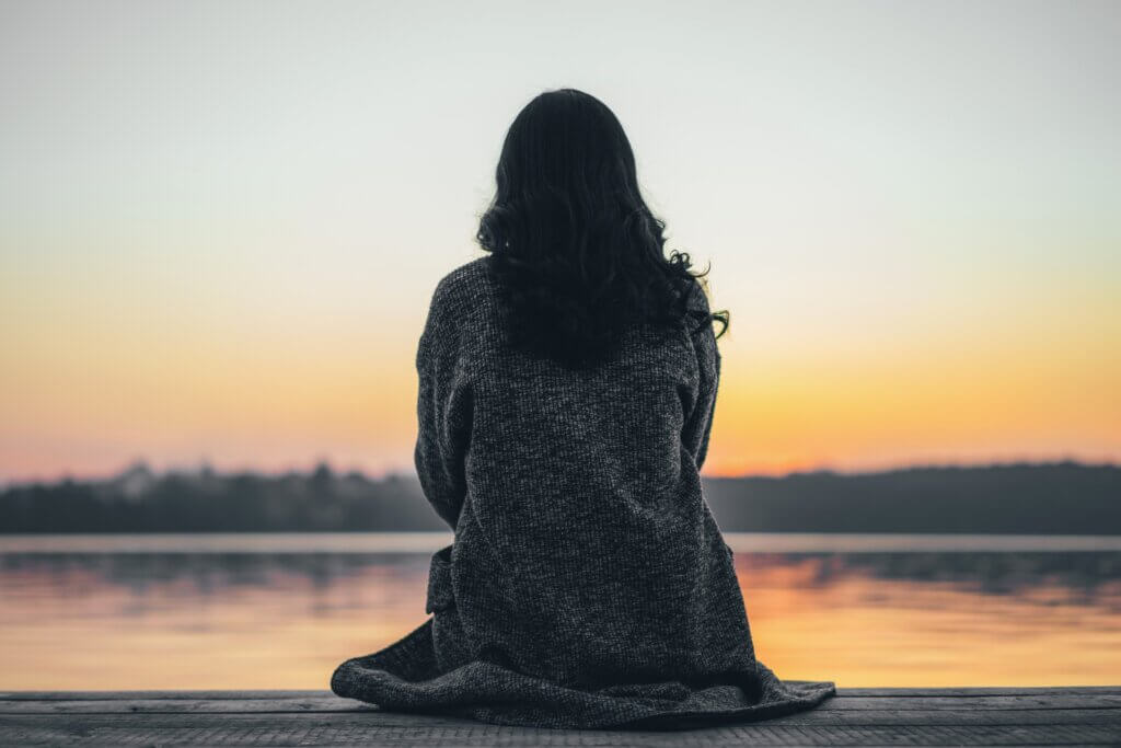 A woman looking out on a lake at sunset.