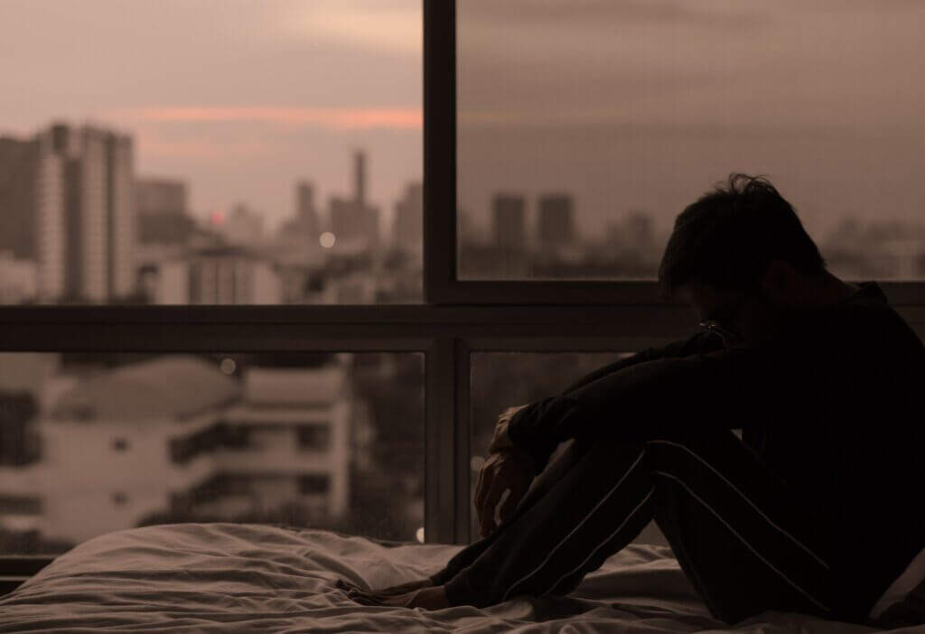 A woman sitting on her bed looking depressed.
