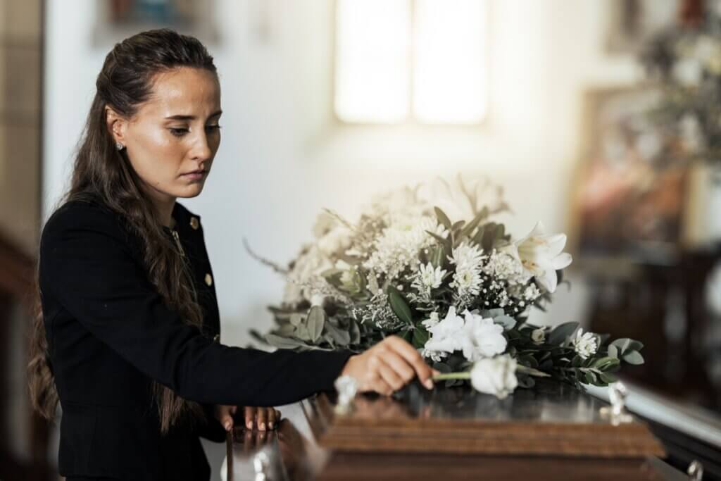A woman dressed in a black dress placing a flower on a casket.