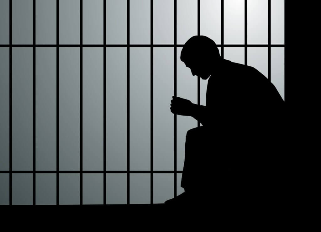 A man sitting alone in a prison cell.