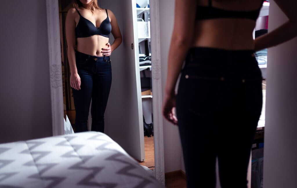 A woman looking at her figure in the mirror.